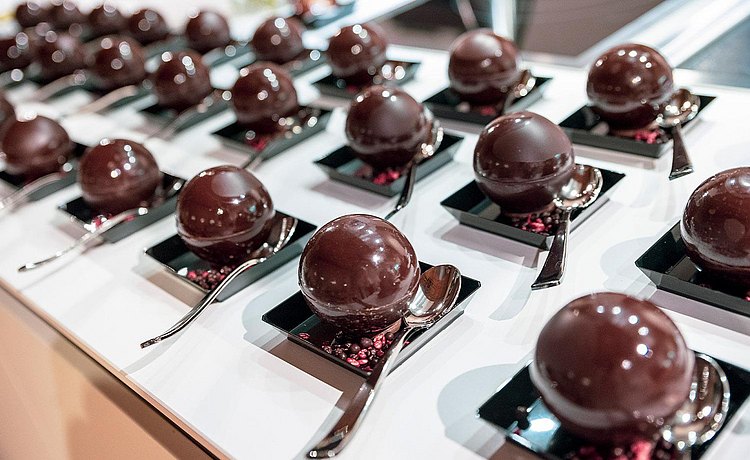 Chocolate confections on small plates laid out on a white countertop.